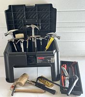Front view of open Rubbermaid step stool toolbox containing seven hammers, rubber mallet, pry bar, carpenter's level, and tool tray with handsaw and utility knives