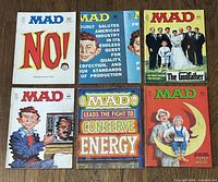 Six Mad Magazines from the early 1970s arranged in two rows on a wood surface, showing full front covers with various colorful and satirical artwork.