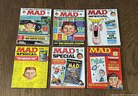 Full view of all 6 vintage MAD magazines arranged on a wooden surface