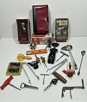 Photo showing assorted vintage corkscrews, bottle stoppers, openers, measuring pourer, a book, and various barware components.