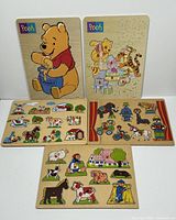 Five wooden puzzles arranged: two Disney Winnie The Pooh puzzles vertical with Pooh holding honey pot and Pooh with friends birthday scene; three smaller farm and circus themed wooden puzzles with chunky pieces.