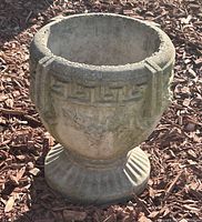Concrete Grecian-style garden planter shown outdoors with visible weathering and moss.