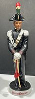 Front view of a ceramic soldier decanter dressed in black and white uniform holding a sword, marked 'Liquore Galliano' at base.