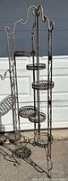 Front view of the vintage metal folding plant stand showing all six planter holders with ornate curved metal design and patina.