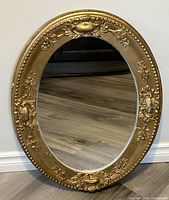 Full view of the vintage oval mirror showing ornate gold gilt carved frame and reflective glass surface.