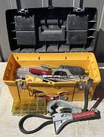 Opened yellow plastic ZAG toolbox displaying assorted hand tools inside and some tools laid on the table beside the box.