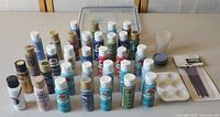 Entire acrylic paint set showing 27 bottles, brushes, palette, and cups arranged on a table