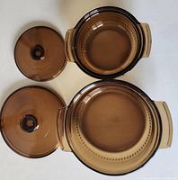 Top-down view of two amber glass casserole dishes and their matching lids placed separately, showing the round shapes and built-in handles.
