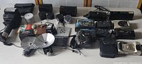 Wide view of all cameras, flash units, film canisters and accessories on a white table surface.