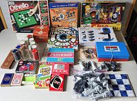 Wide shot showing the collection of card and board games plus game accessories laid out on a table including boxed board games, card decks, poker chips, and chess pieces.