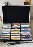 Open black carrying case showing 26 country music cassette tapes arranged in five rows.