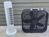 Photo of two electric fans: a white tower fan and a black box fan placed side by side outdoors.