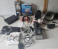 Various electronics displayed on a table including headphones, a GPS device, boxed Sony Dream Machine calculator, Avantree Bluetooth transmitter in packaging, and numerous wires and adapters.