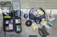 Overview of assorted fasteners, hardware pieces, tools, and storage containers arranged outdoors on a concrete surface.