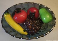 Top view showing carnival glass bowl with five colorful glass fruit figurines inside: banana, apples, grapes, and pear.