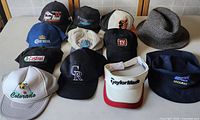 Photo showing 12 hats including various baseball caps and one grey fedora