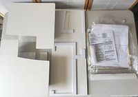 Top-down image showing white plastic frame components and plastic-wrapped paper templates with instructions.