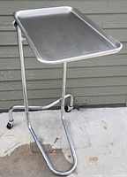 Front angle view of the stainless steel Mayo instrument stand showing the tray, U-shaped wheeled base, and height adjustment knob.