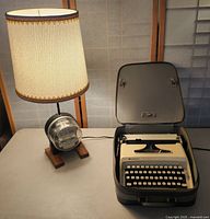 Full view of Remington Ten Forty typewriter in carrying case and the electric meter lamp with white lampshade on a table.
