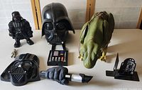 Photo showing all items in the lot: Darth Vader full helmet mask, Darth Vader hand holding lightsaber, Darth Vader robot action figure, Jabba the Hutt figure, pilot figure, and R2-D2 bookend.