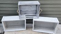 Three whitewashed wooden storage crates displayed outdoors against a brown siding wall, showing different styles and finishes.