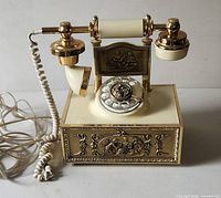 Front view of vintage French rotary dial phone with brass decorations and ivory body, showing coiled cord and handset.