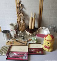 Wide view of various vintage kitchen items arranged together including rolling pins, cookie jar, utensils, wooden wall hanging.