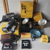 Photo showing vintage Kodak camera, flash attachments, boxes with Kodak branding, film bulb box, cleaning papers, and photography guide booklet.