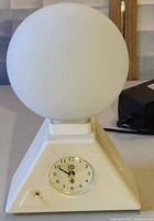 Overall view of the vintage sunrise alarm clock featuring a white plastic body and frosted glass globe on top.
