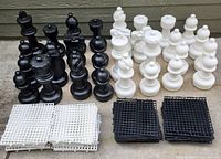 Full set of extra large black and white plastic chess pieces arranged with matching black and white grid base tiles beneath.