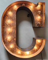 Front view of the large metal letter C illuminated by light bulbs.