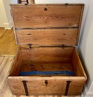 Open lid showing interior of solid pine wooden trunk with some wear marks, blue cloth inside.