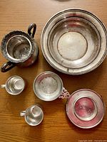 Overhead shot of two Lennox pewter cups, Schwarzchild pewter bowl, Vanbergh silver-plated sugar bowl and Gotham sterling silver bowl on wood table