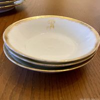 Set of three small white bowls stacked showing gold rim and gold letter R interior detail.