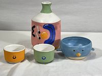 Photo of two small ceramic smiley face bowls, a blue bird-shaped bowl, and a hand painted vase.