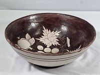 Oval pottery bowl with dark brown glaze and white fruit and leaf hand painted designs inside.