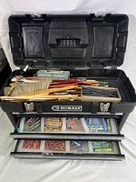 Full view of open Kobalt toolbox showing paintbrushes in top compartment, charcoal sticks in a small box, and colorful pastel sticks in two pull-out drawers.