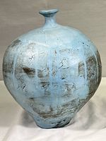 Front angle profile of rustic round ceramic vase showing blue matte glaze with brown and grey textured areas and vertical light blue streaks.