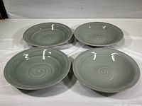 Set of four light green ceramic pasta bowls with a spiral swirl design