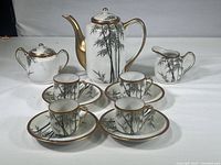 Full view of the entire vintage Asian porcelain tea set with cups, saucers, pitcher, sugar dish, and creamer decorated with bamboo and gold accents.