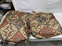 Two folded sections of multicolor floral patterned fabric in reds, blues, tan, and golds.