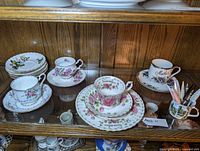 Display of multiple teacups and saucers inside glass case showing floral patterns and calendar design.