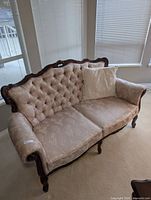 Full view of the baroque style loveseat highlighting tufted back and carved wood frame with white lace-trimmed accent pillow.