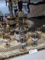 Overall lot showing glass decanter and eight sherry glasses set on a crochet lace doily.