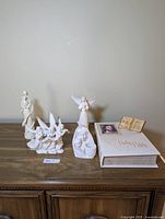 Wide view of the entire lot showing all four angel sculptures and the large ceramic Holy Bible with open book decoration, displayed on wooden surface.