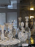 View of all crystal decanters and vases arranged on crocheted doilies with reflective mirror background
