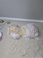 Pile of various vintage crocheted doilies in pastel shades laid on floor, showing intricate lacework and handmade patterns.