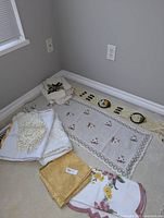 Embroidered tablecloth laid flat showing floral patterns and lace border with surrounding folded lace and linens.