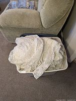 Large plastic tote filled with multiple white lace tablecloths with floral lace pattern, folded and layered inside.