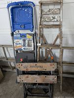 Ladders, step stools and Black & Decker folding workbench stacked upright showing worn conditions and paint marks